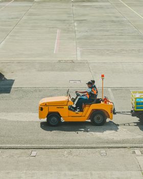 An airport ground vehicle towing luggage on the apron on a sunny day.