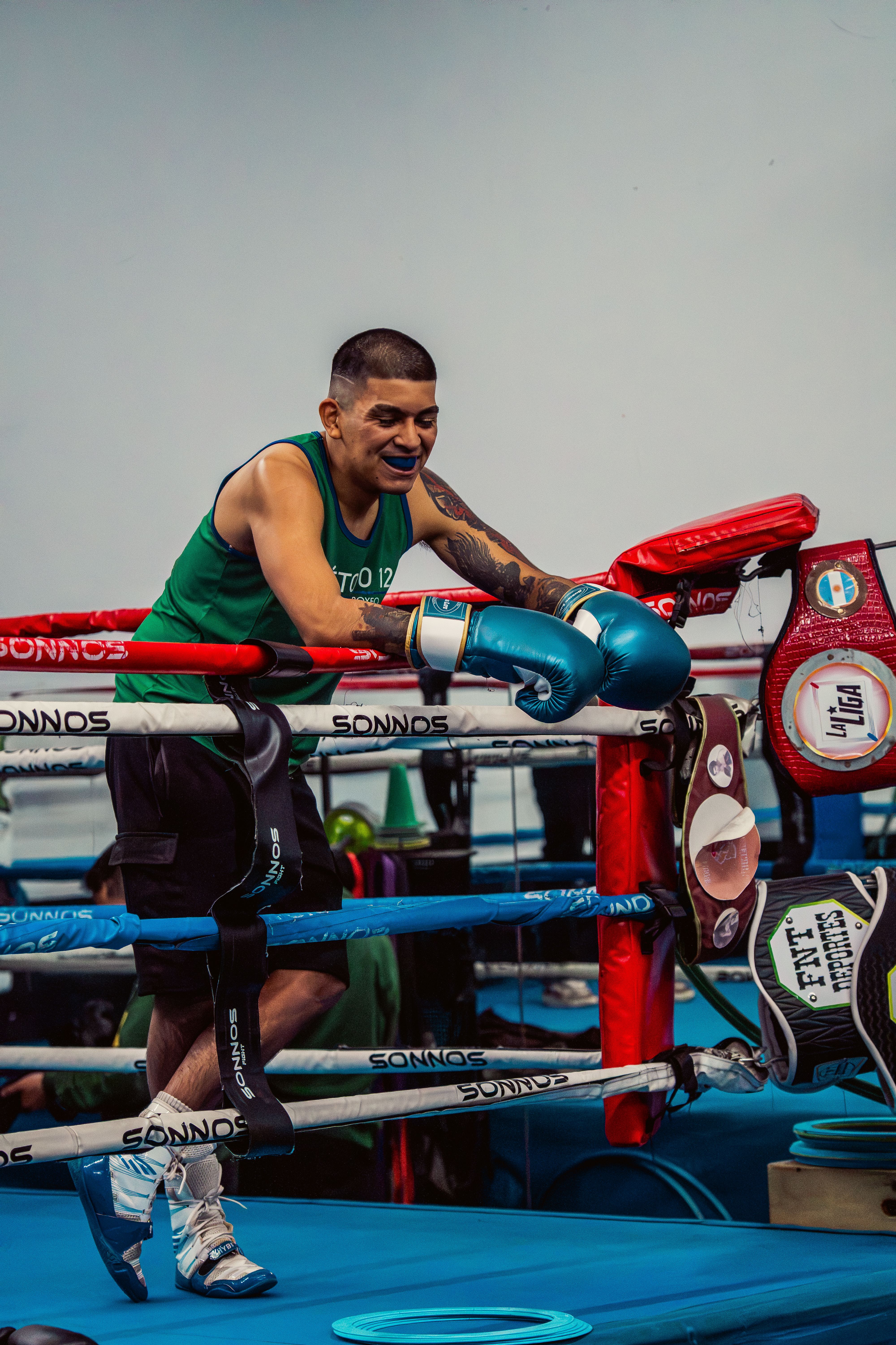 A boxer rests against the ropes in a gym, ready for the next round.
