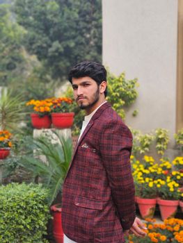 A stylish young man poses confidently in a vibrant garden setting with blooming flowers.