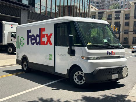 Electric FedEx delivery truck parked on an urban street in daylight.