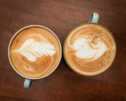 Top view of two lattes with intricate latte art designs, set against a wooden table background.