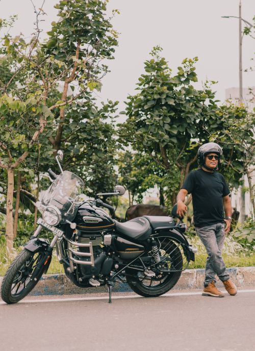 Free A man in Kolkata wearing a helmet, leaning on a parked motorcycle under trees, conveying a relaxed vibe. Stock Photo