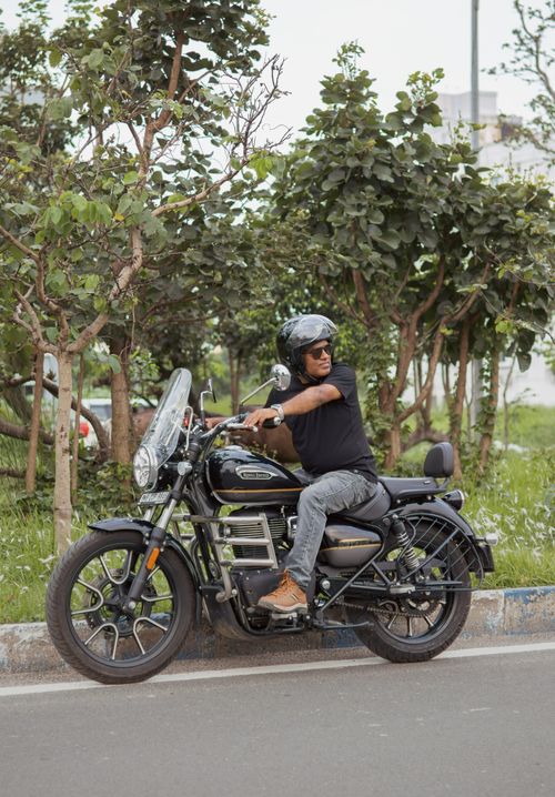 Free Person on motorcycle stopped on a city street surrounded by trees in Kolkata, India. Stock Photo