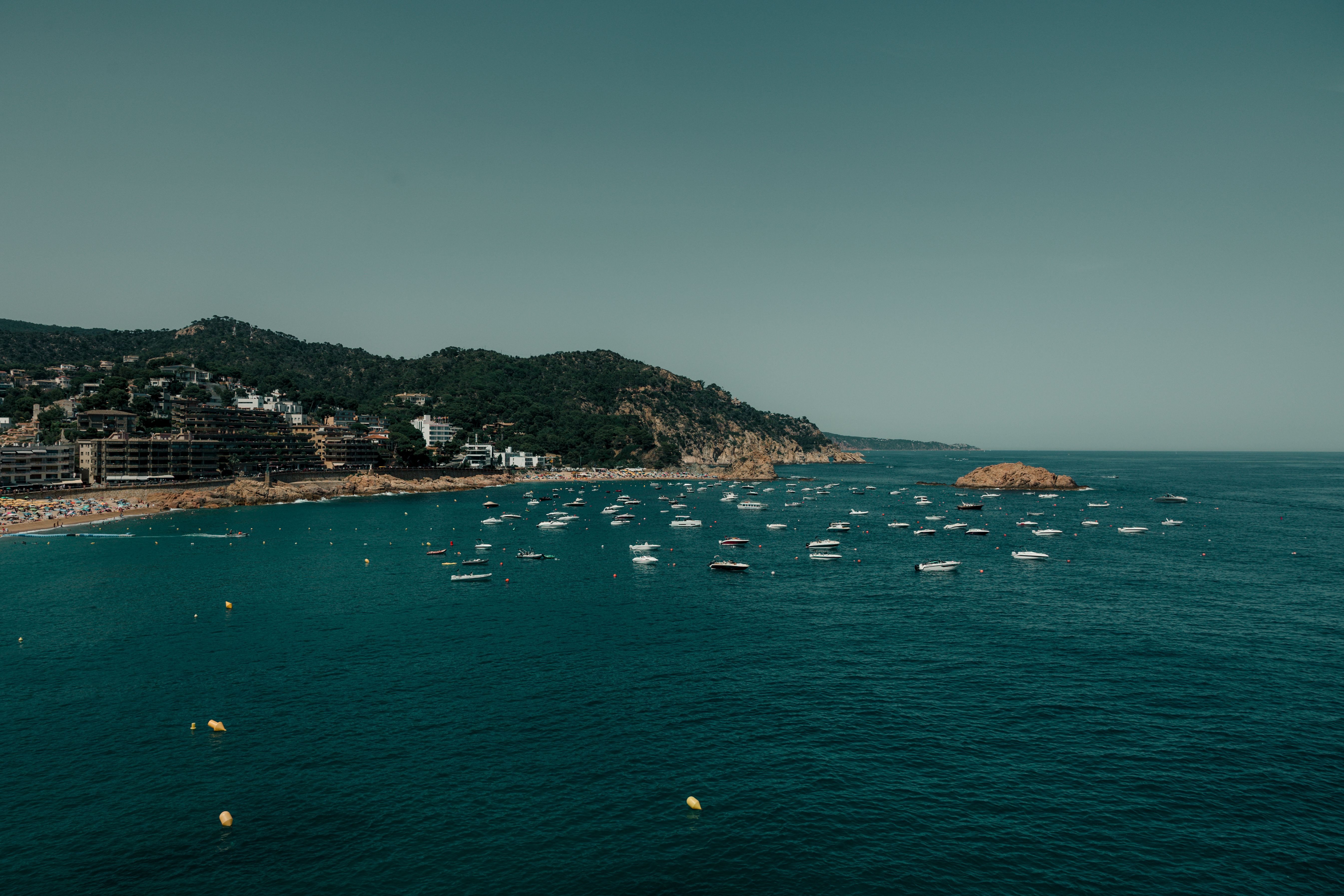 A picturesque view of Tossa de Mar's coastline featuring boats and lush landscapes under a clear sky.