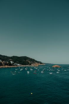 A picturesque view of Tossa de Mar's coastline with boats on the turquoise waters under a clear sky.