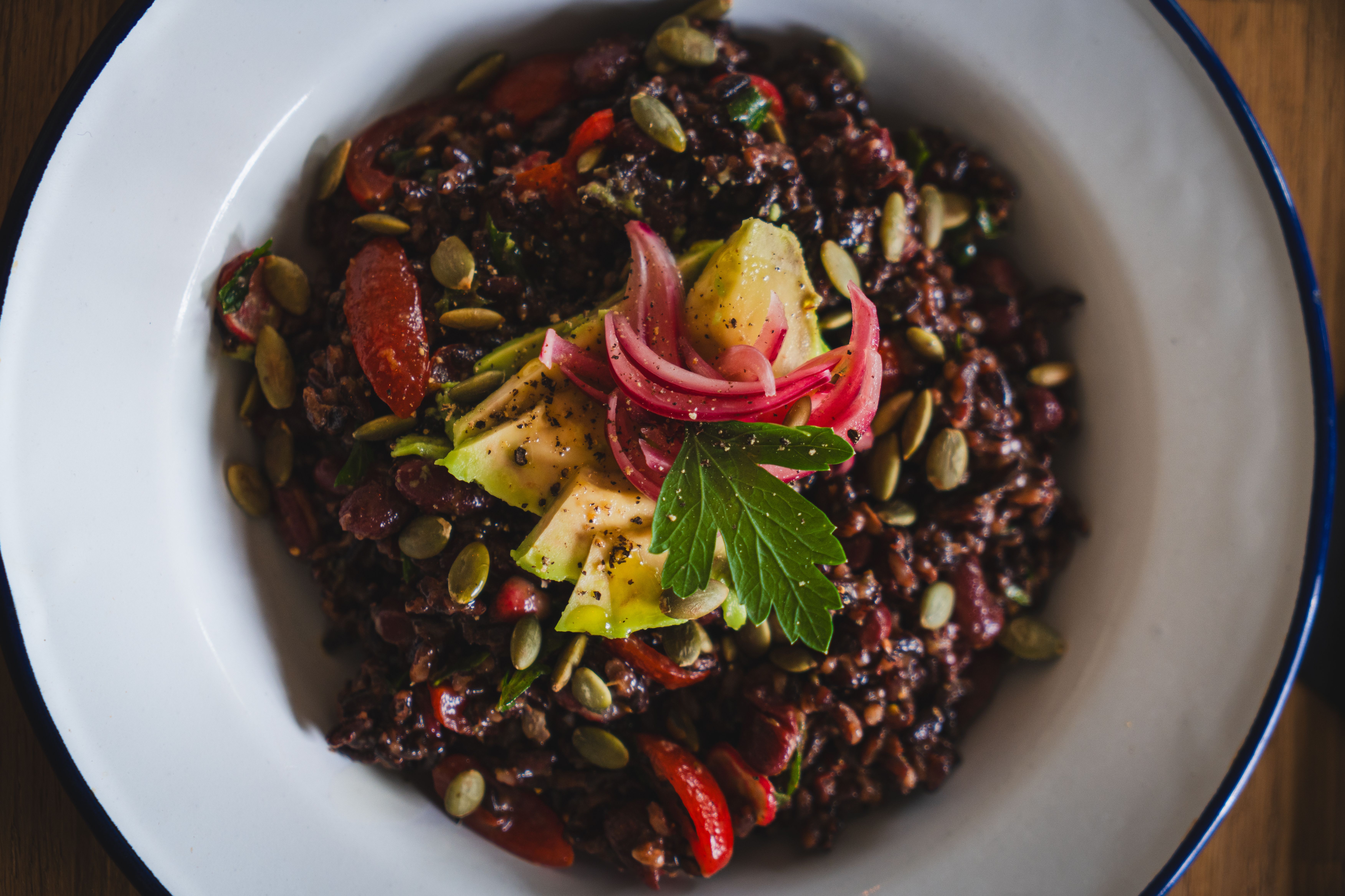 Healthy vegan black rice salad topped with avocado, pickled onions, and pumpkin seeds.