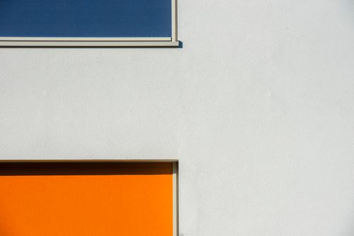 Free A minimalist architectural facade featuring bright orange and blue geometric elements. Stock Photo