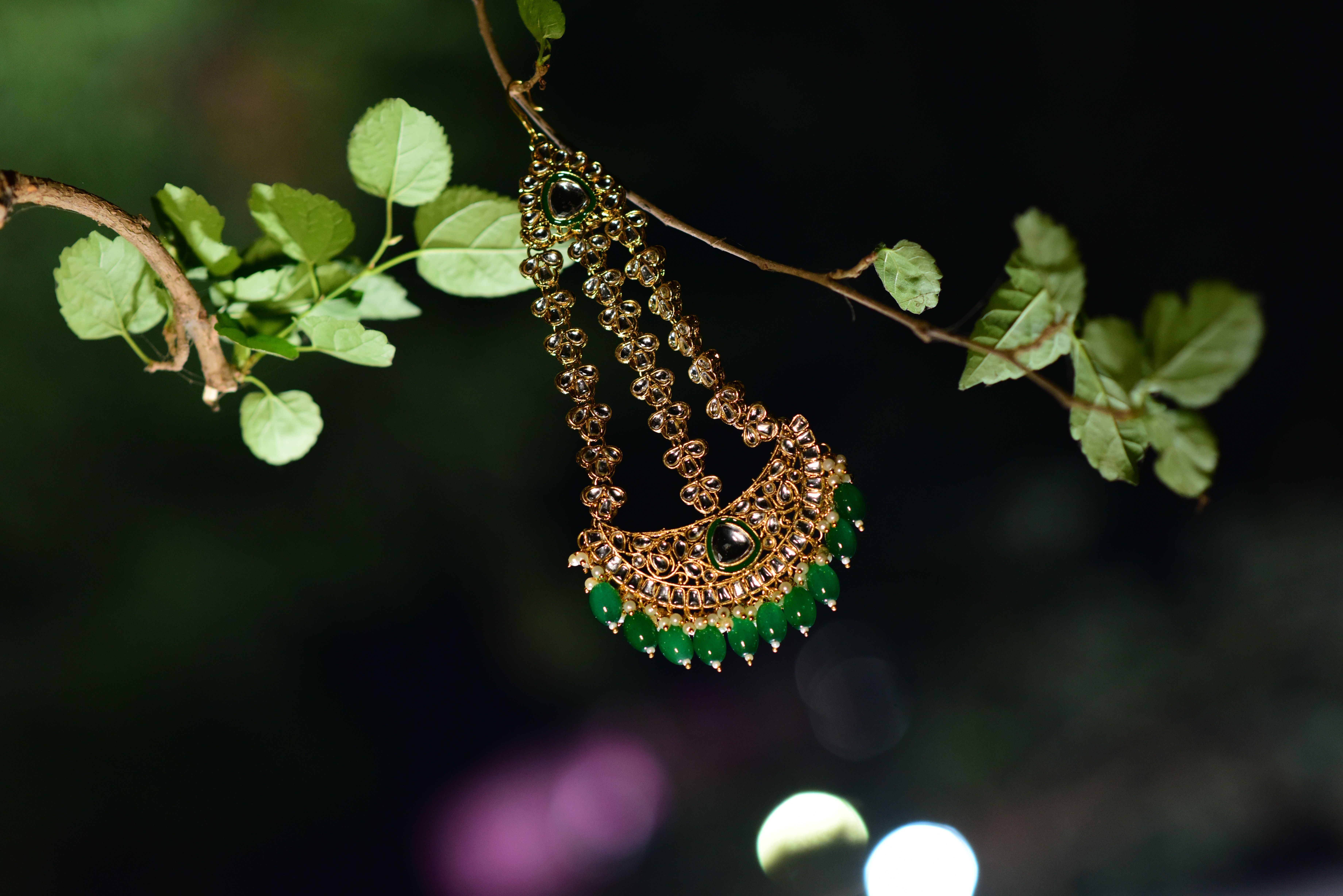 Delicate organic-patterned gold necklace featuring rich green emeralds hanging gracefully on green branch