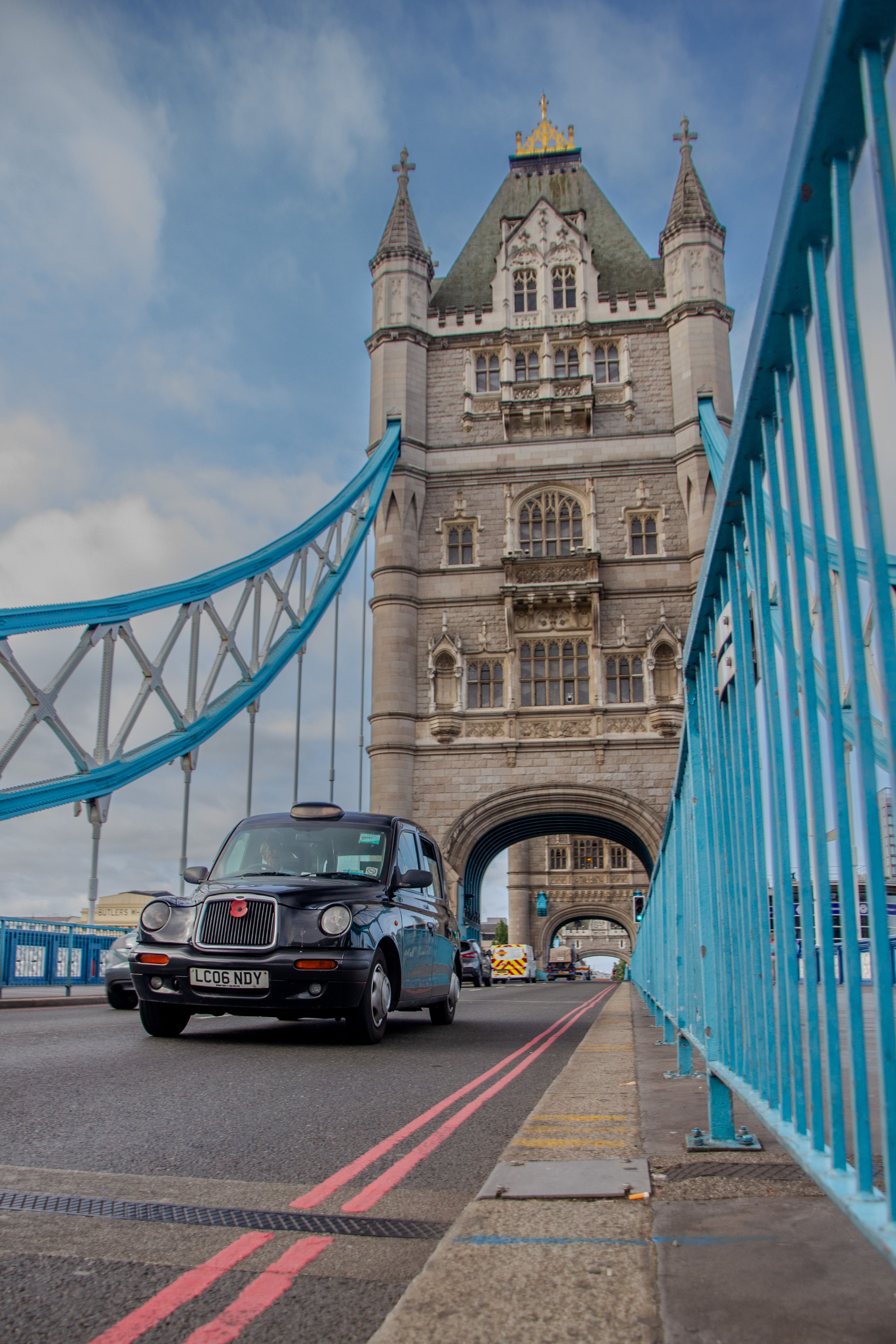A classic black taxi crossing Tower Bridge in London, iconic landmark under a clear sky.
