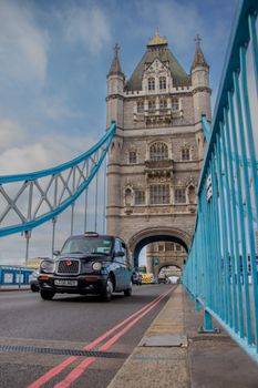 A classic black taxi crossing Tower Bridge in London, iconic landmark under a clear sky.