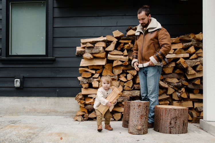 Cheerful Father And Kid With Firewood Near House