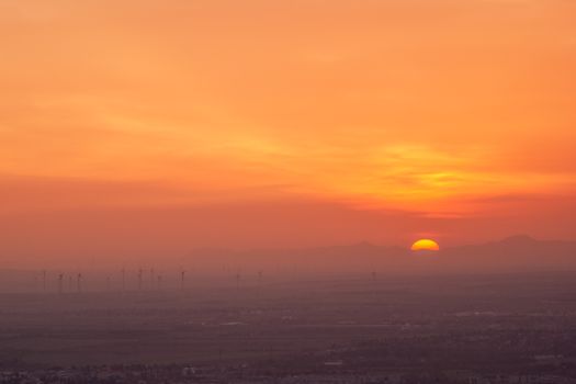 A vivid sunset over a landscape with wind turbines silhouetted against an orange sky.