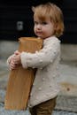 一个可爱的幼儿穿着舒适的毛衣，在户外拿着木头，天真而迷人