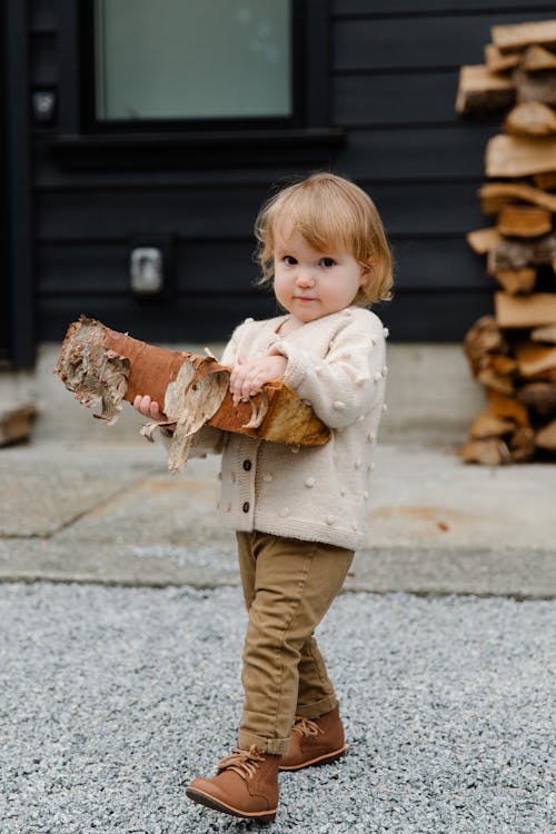 Funny kid with firewood walking in yard