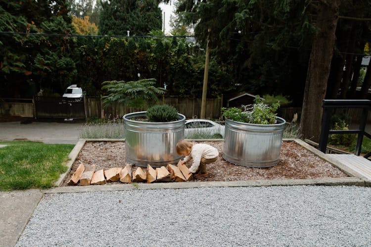 Little Child Playing With Firewood In Garden