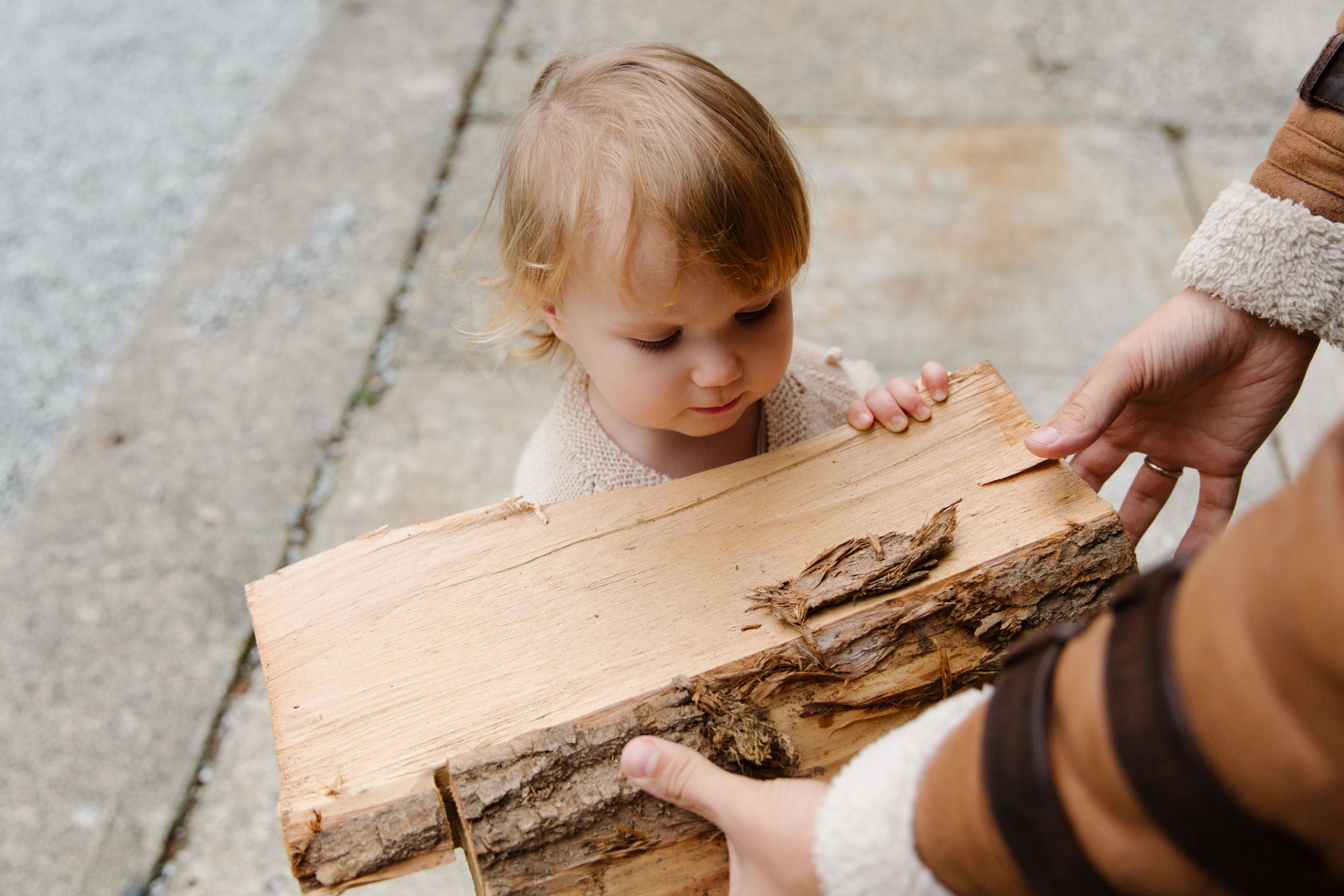 A cute little girl assisting in carrying firewood outdoors during summer.