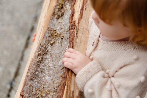 From above of little girl standing with firewood looking away and thinking while spending time in countryside during weekend and enjoying