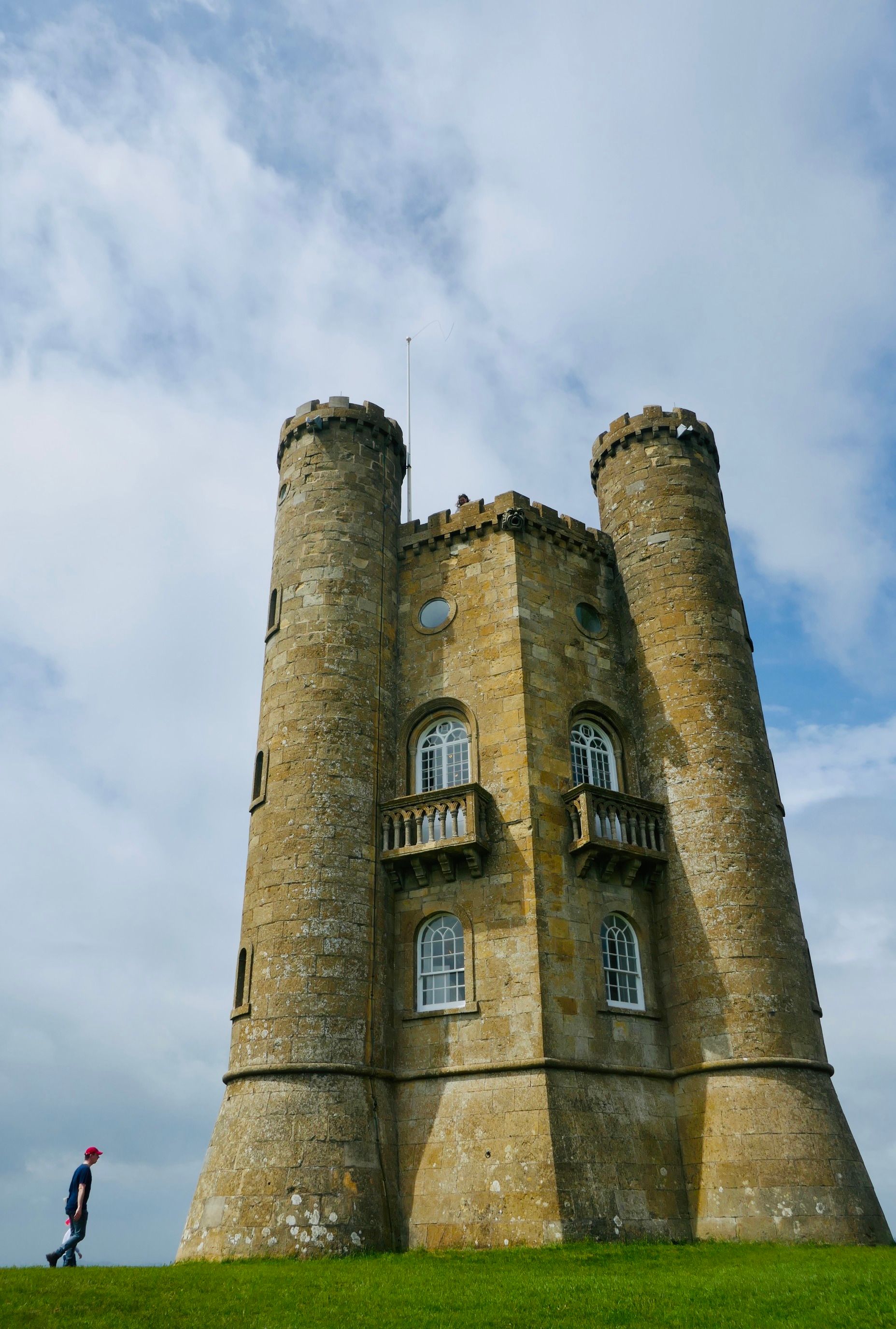 A striking medieval tower stands under a cloudy sky on a lush green hill.