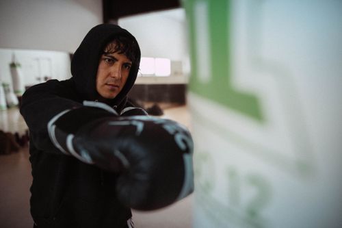 Free Boxer in black gloves punching heavy bag indoors, Buenos Aires gym. Stock Photo