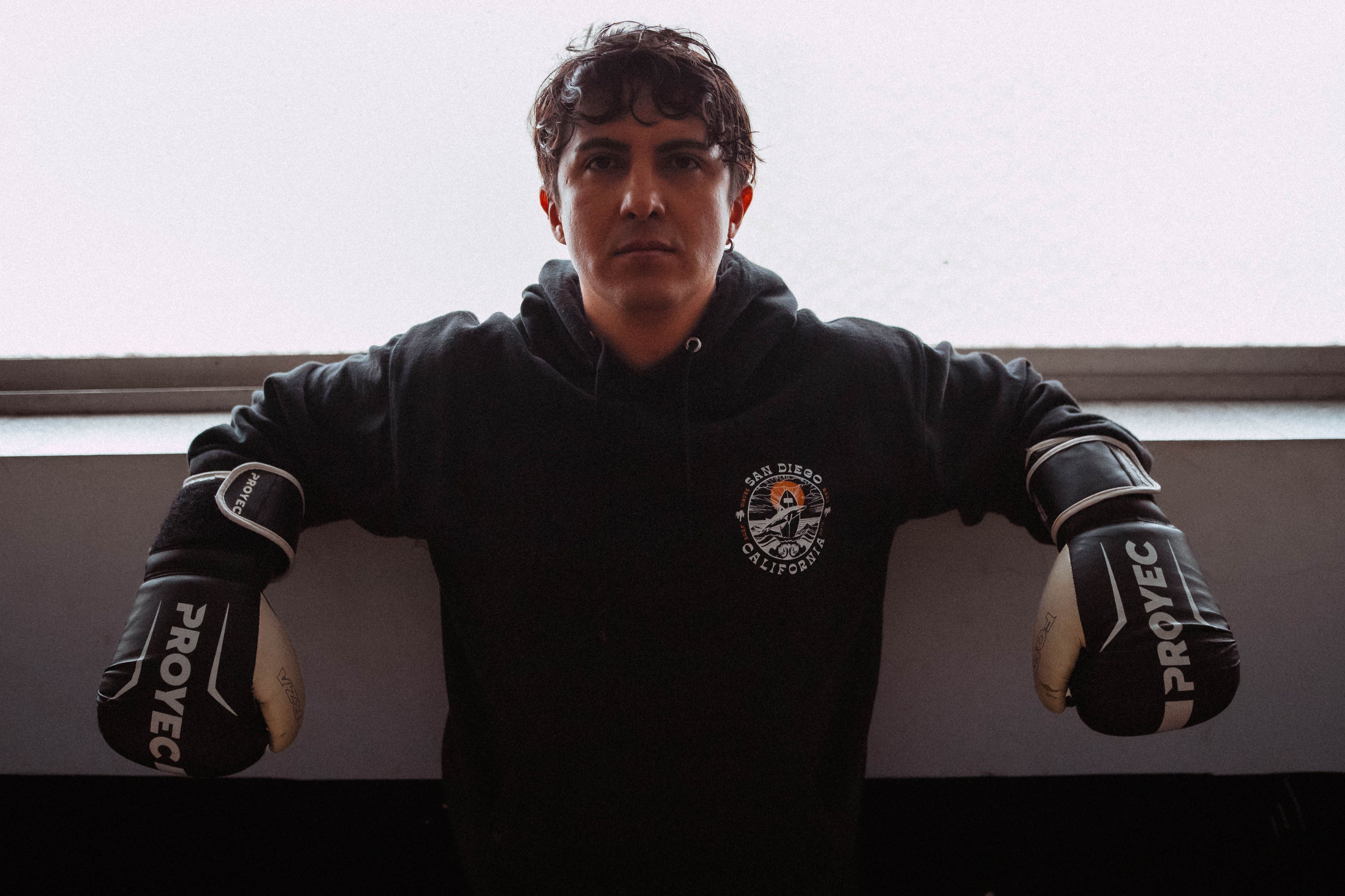 Boxer in Proyec gloves standing confidently indoors with gym apparel.
