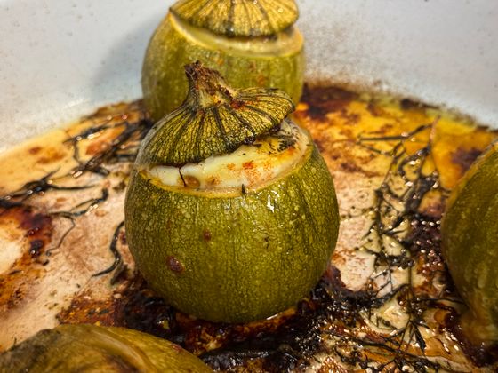 Round zucchini with lid stuffed with golden cheese filling roasted in a pan with thyme