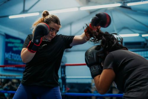 Free Two women engaging in a fierce boxing match inside a gym, showcasing strength and determination. Stock Photo