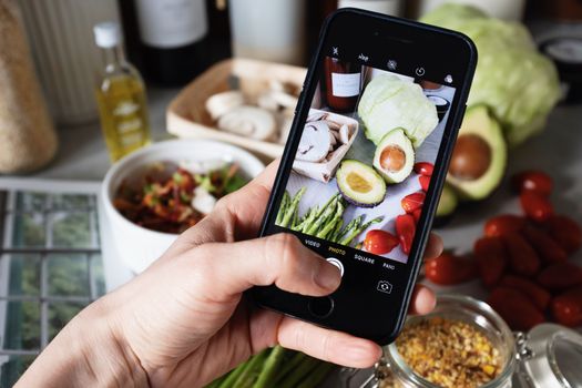 Photographing a healthy meal setup with various fresh vegetables using a smartphone.