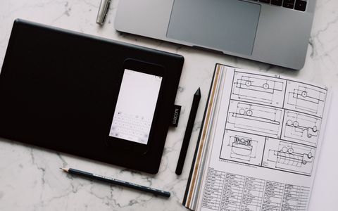 A minimal desk workspace with a laptop, drawing tablet, and design documents laid out