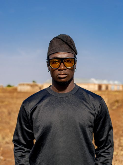 Free Portrait of a man in stylish attire with sunglasses and cap in a rural setting. Stock Photo
