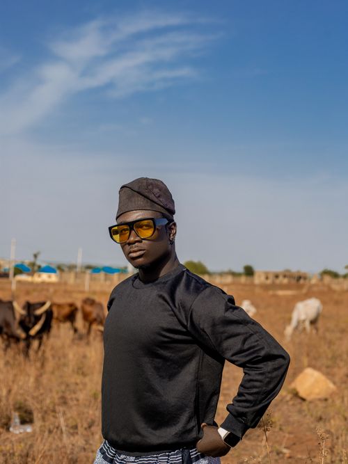 Free A confident young man in sunglasses poses outdoors with cattle in the background, showcasing rural life. Stock Photo