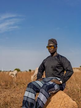 Man in traditional attire posing outdoors with clear blue sky.