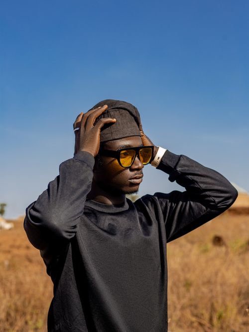 Free Young man wearing sunglasses and hat in a dry, open landscape under a clear blue sky. Stock Photo