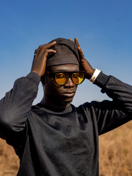 Free Man in stylish black outfit and sunglasses posing in sunny outdoor setting. Stock Photo