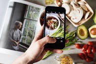 在现代厨房的桌子上，不露面的博主拍摄了白色碗里新鲜美味的沙拉和其他食物的智能手机照片