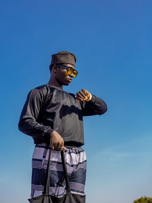 Free Fashionable man wearing sunglasses and hat checks the time with a clear blue sky backdrop. Stock Photo