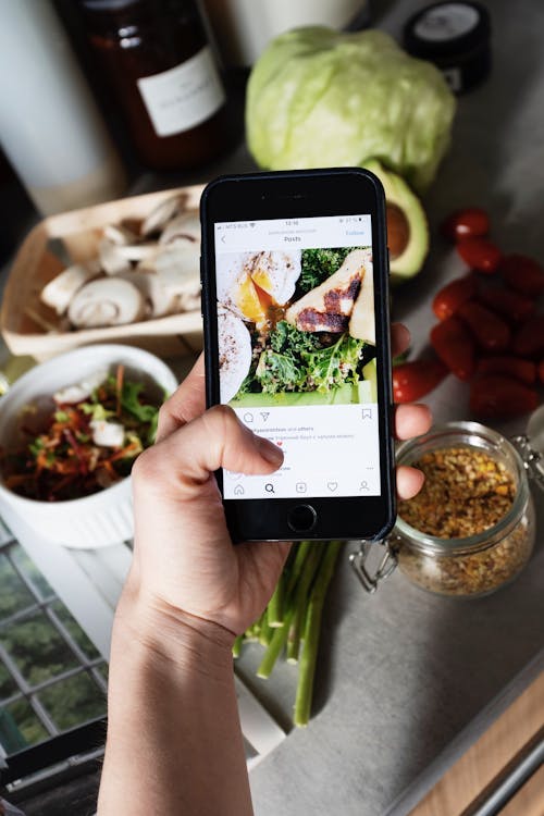 Free From above of crop person touching cellphone screen while searching for image of healthy recipe and standing in kitchen in front of vegetables Stock Photo