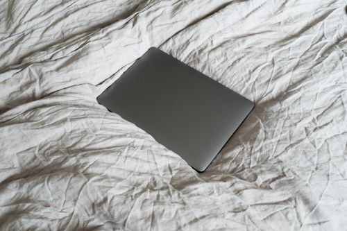 Free From above of closed dark gray portable computer located on large soft and crumpled cotton bed sheet in apartment in light room Stock Photo