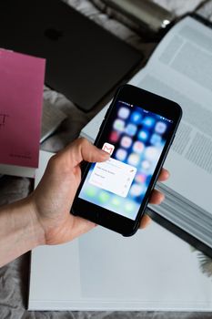 Hand holding smartphone with email app open, surrounded by books and laptop.