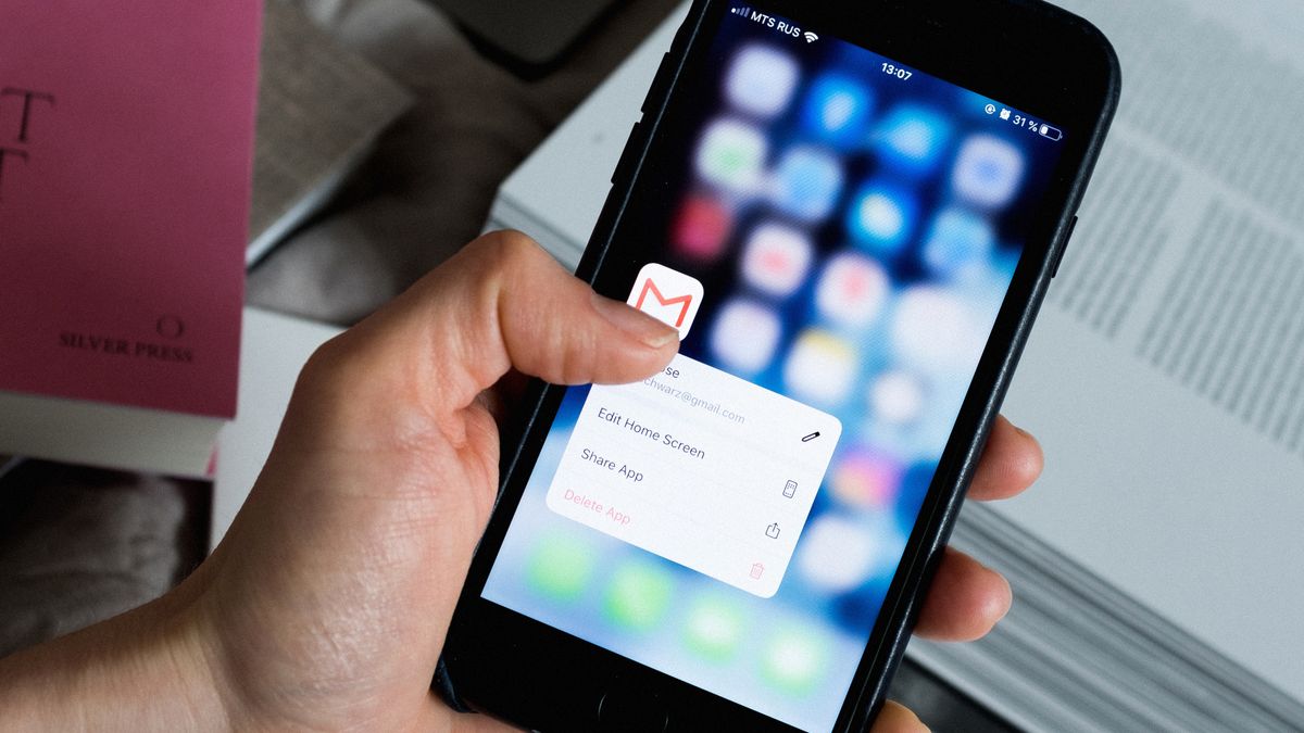 Main tenant un smartphone affichant une messagerie, avec ordinateur sur un bureau