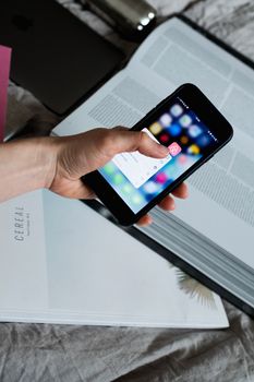 Hand holding a smartphone above an open book with a mobile app displayed on screen.