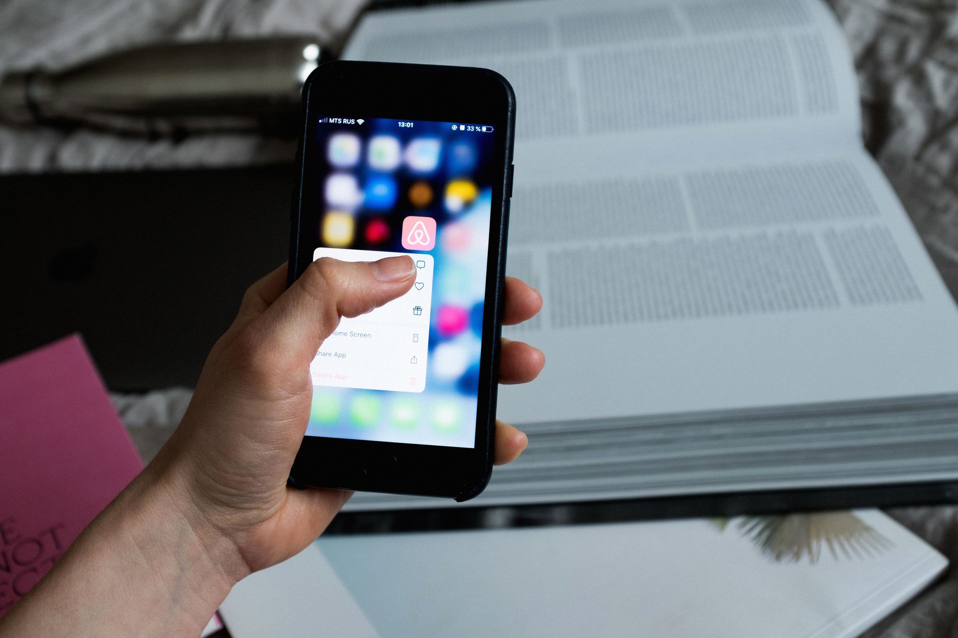 Close-up of hand using smartphone with blurred app icons, open books in the background.