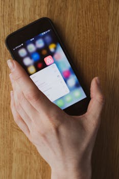 A hand holding a smartphone displaying an app icon on a wooden surface.