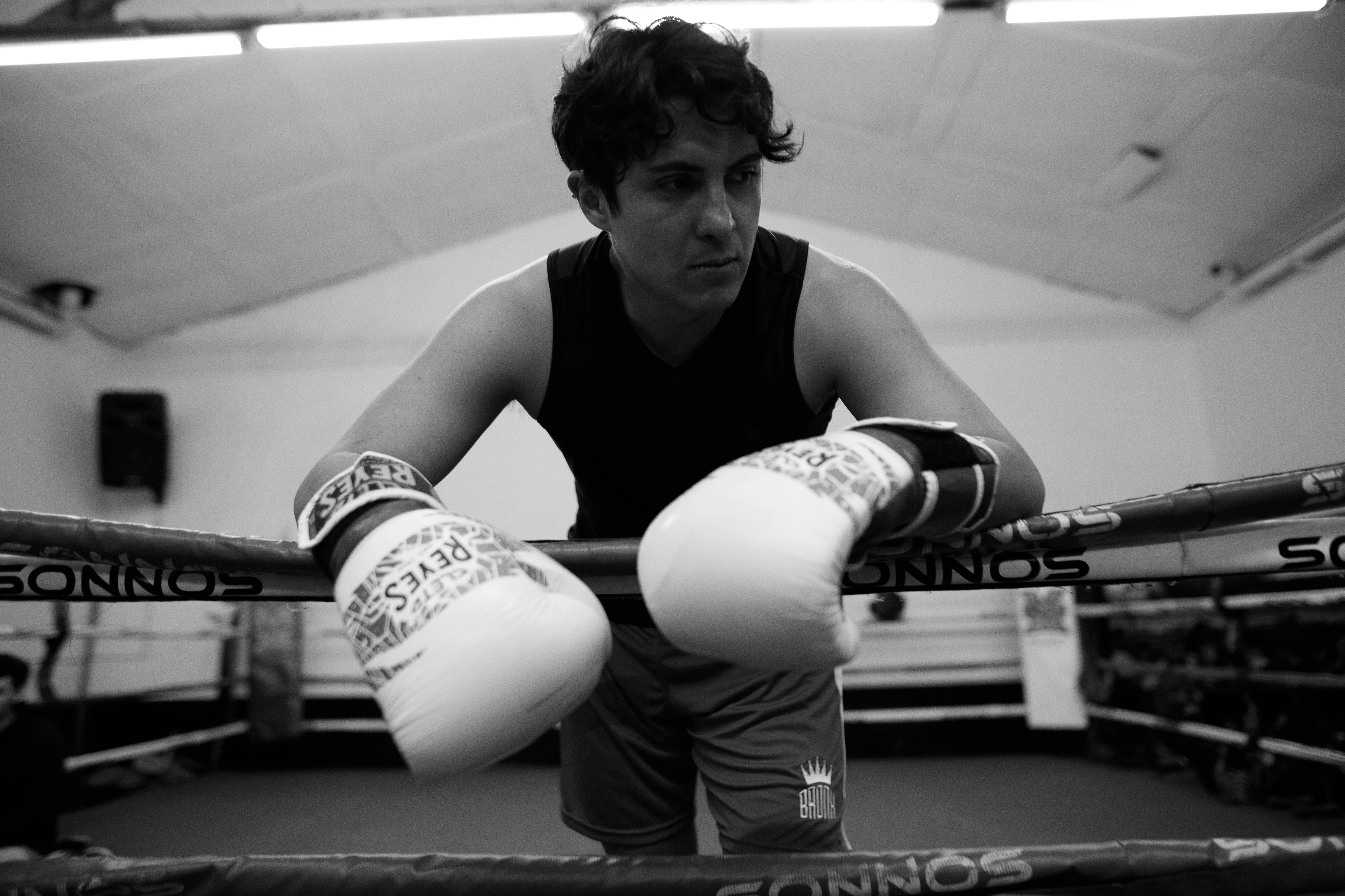 A determined boxer wearing gloves, leaning on boxing ropes during training in Buenos Aires.