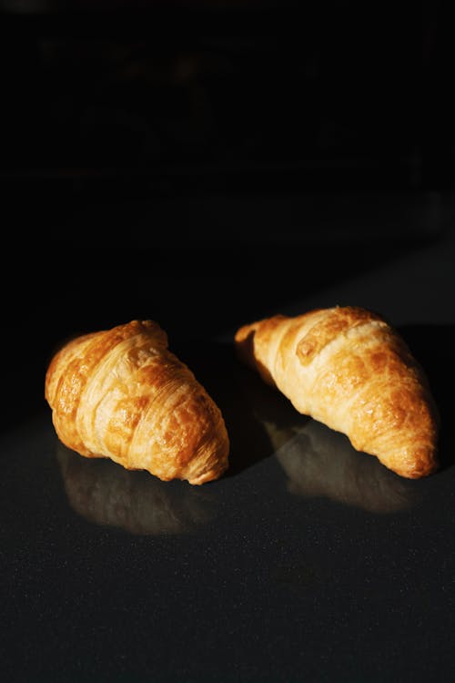 Pair of delicious fresh croissants on black glass background