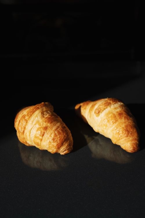 Free Group of two whole baked tasty crunchy croissants placed on black glass surface Stock Photo