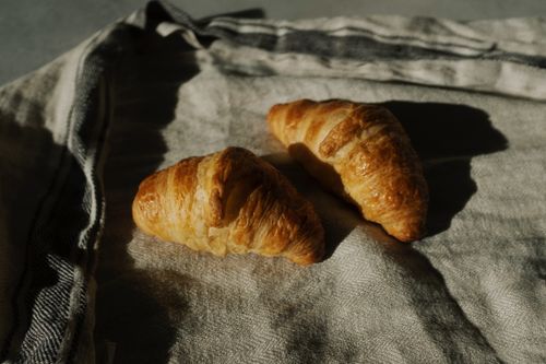 Free Freshly baked croissants resting on a rustic fabric with warm morning light casting shadows. Stock Photo