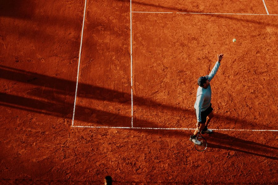 Tennis player serving on a clay court, aerial view