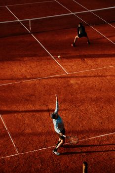 Two players in action during a tennis match on a clay court under natural light.