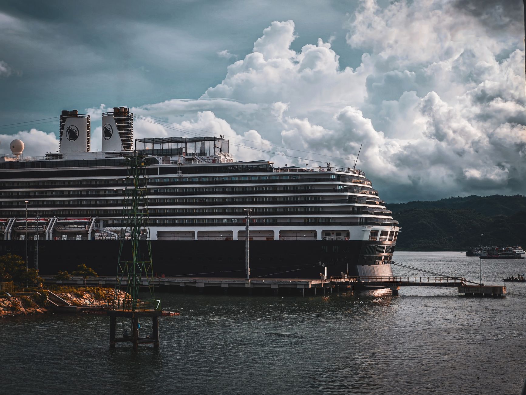Ein großes Kreuzfahrtschiff, das in einem Hafen anlegt, mit dramatischen Wolken im Hintergrund, die eine beeindruckende maritime Szene schaffen.