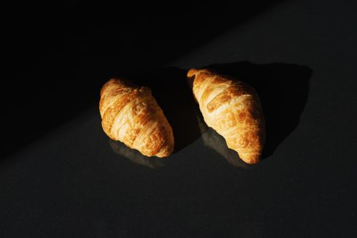 Free Two golden croissants on a dark surface captured in natural lighting, highlighting their flaky texture. Stock Photo